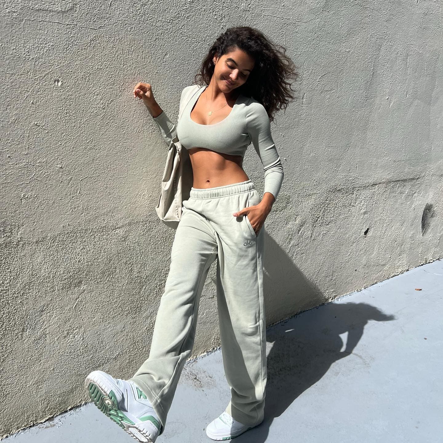 @juliamuniz wearing a pair of straight-leg sweatpants in a light sage color with a matching ribbed long sleeve bra top while walking down a sidewalk.  