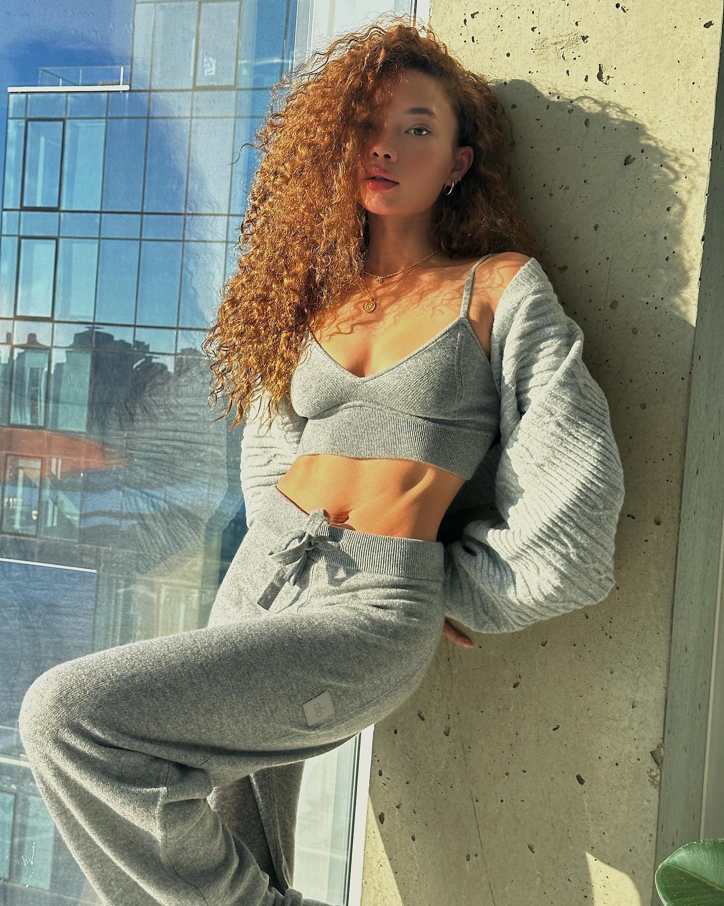 @ashley_moore_ wearing a cashmere bra top with a pair of cashmere wide-leg pants and a knit shall over the top while posing against a concrete pillar next to a skyrise window. 