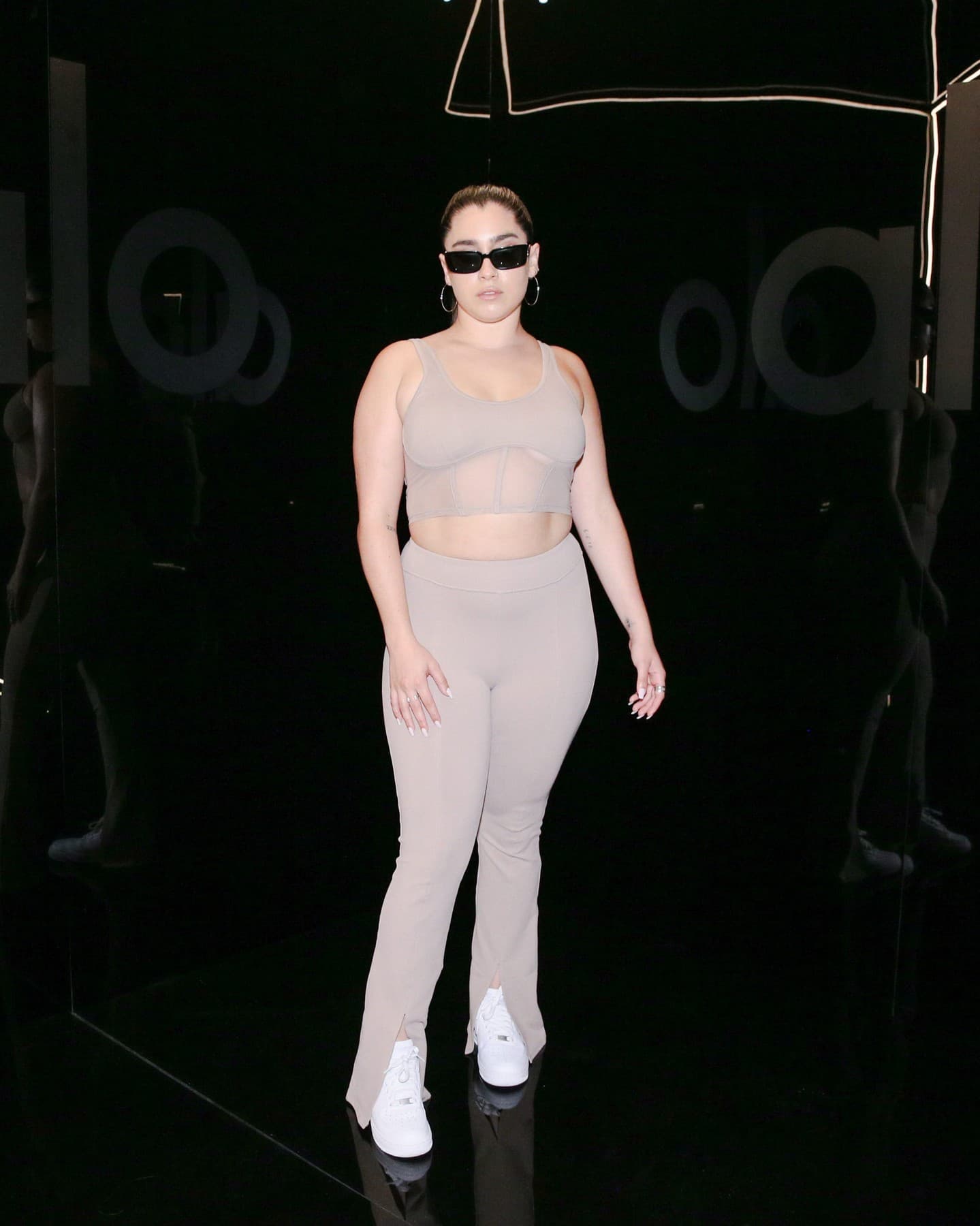 @laurenjauregui wearing a pair of taupe-colored flared leggings with a split hem along with a matching corset bra tank while posing for a picture at Alo’s NYFW presentation of the Aspen Collection.