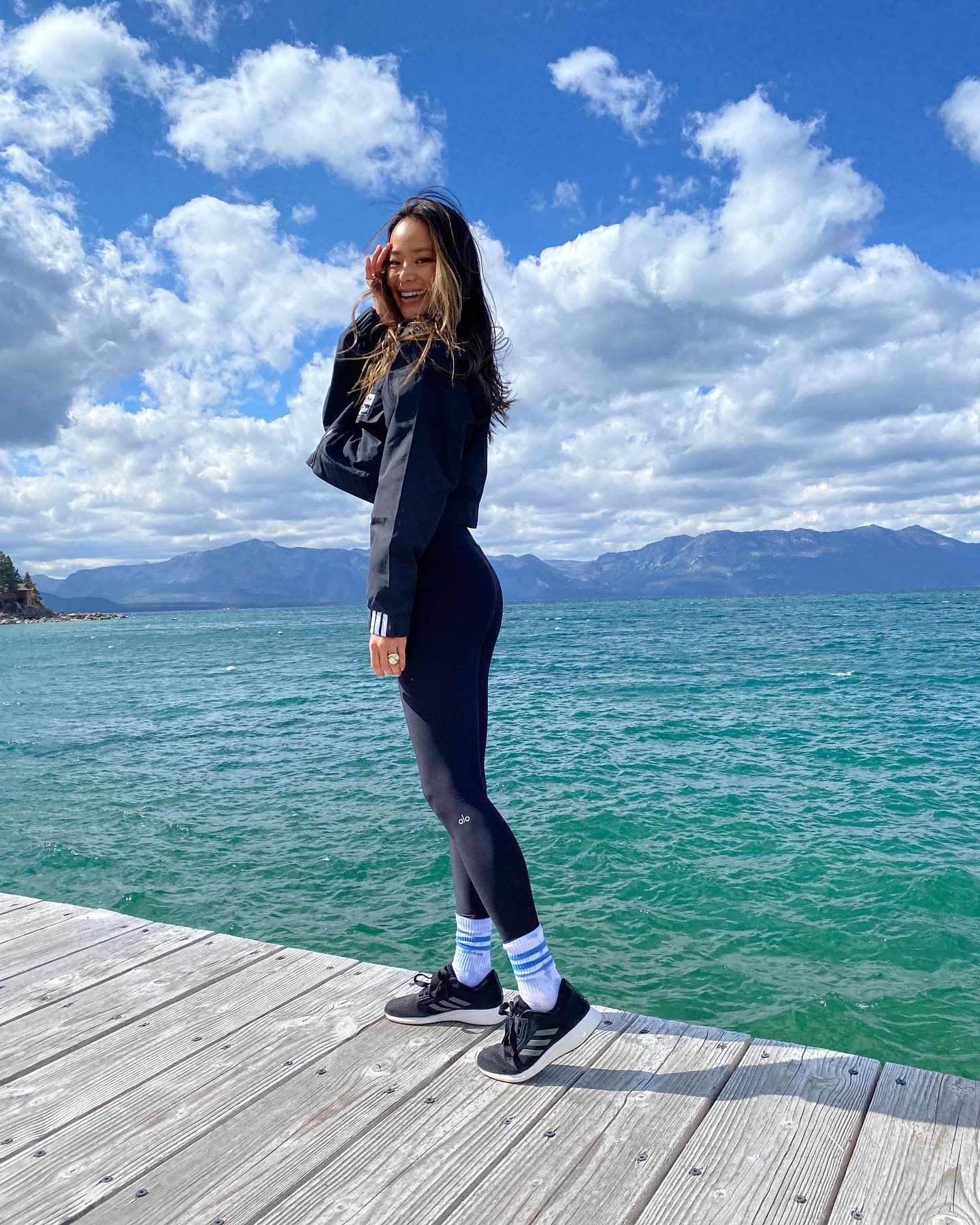 Jamie Chung wearing a pair of Black High-Waist Airlift Leggings with a cropped sweatshirt, crew socks, and sneakers while posing on a dock at Lake Tahoe.  