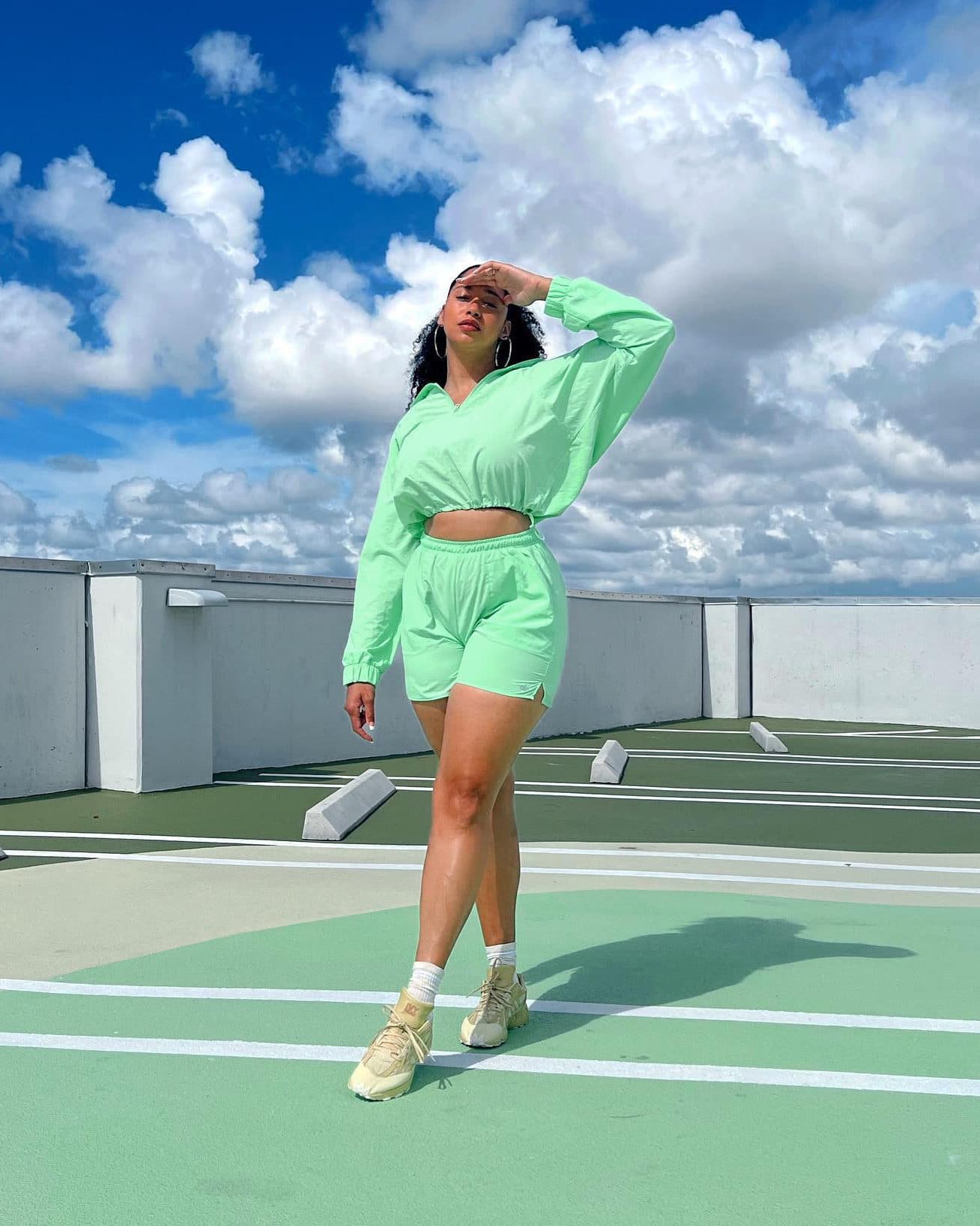 @torianicholexoxo wearing a crinkle fabric short and quarter zip jacket set while standing on a rooftop parking lot with a bright blue sky full of fluffy white clouds in the background.  