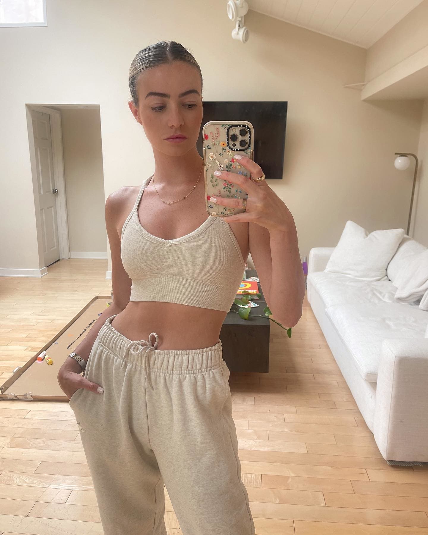 @ewebbz wearing a comfy lounge sports bra in an oatmeal color with a pair of matching sweatpants while taking a mirror selfie in her living room.  