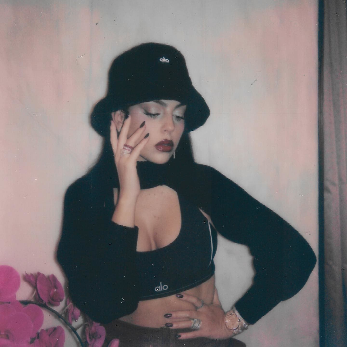 @georginagio wearing an black Alo sports bra with white contrast piping with an ultra-cropped shrug over the top and a faux fur bucket hat while posing against a wall.  