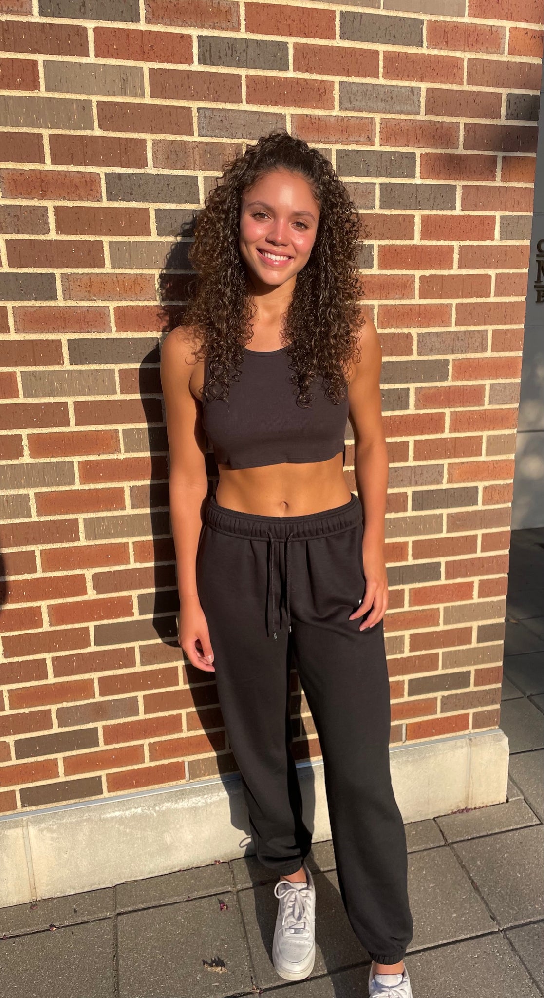 Zairyn Hemsley wearing Accolade Sweatpants and a Ribbed Vibe Tank both in Black while posing in front of a brick wall.  