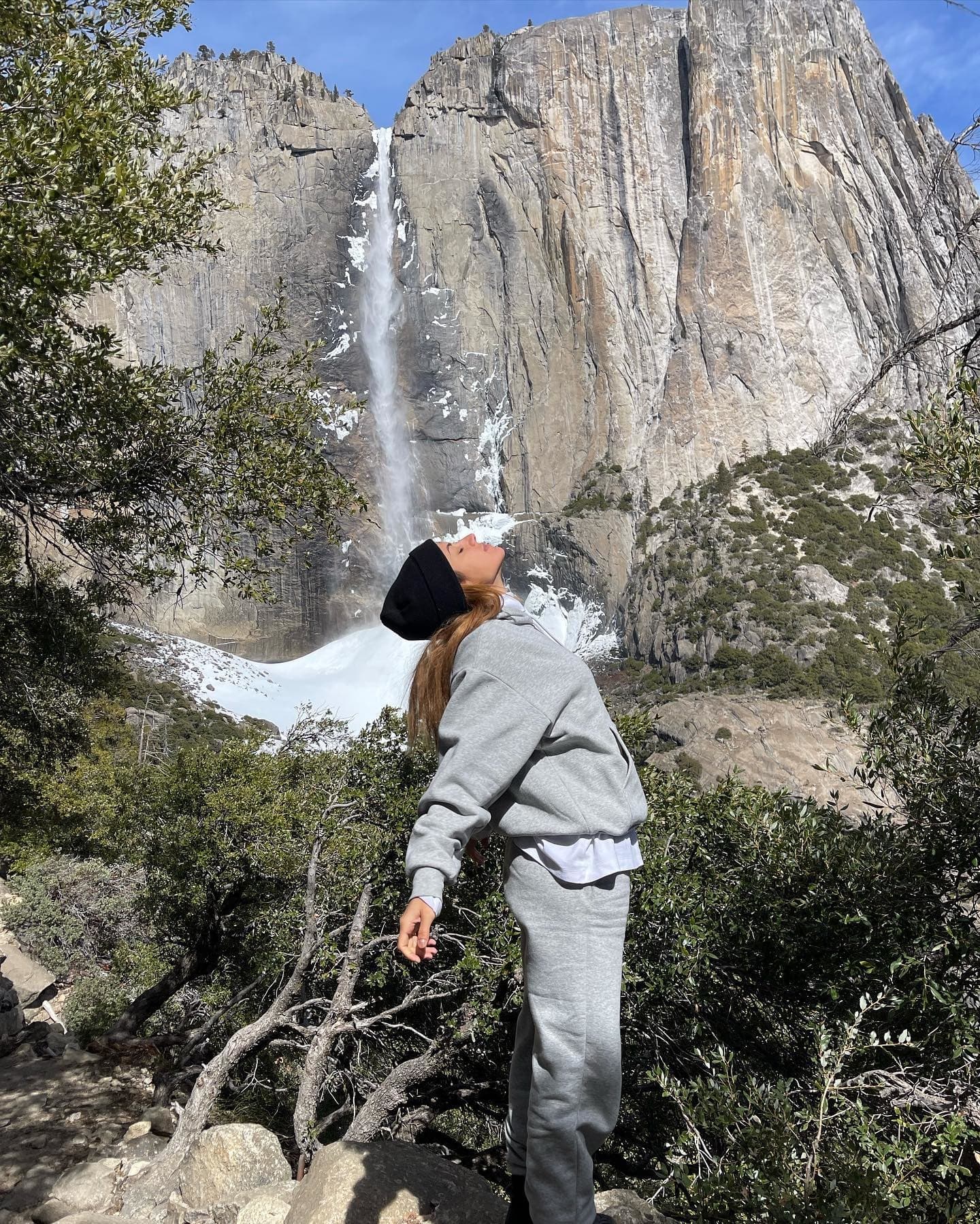 @inanna wearing a light grey sweat set while posing in front of large waterfall in the forest.  