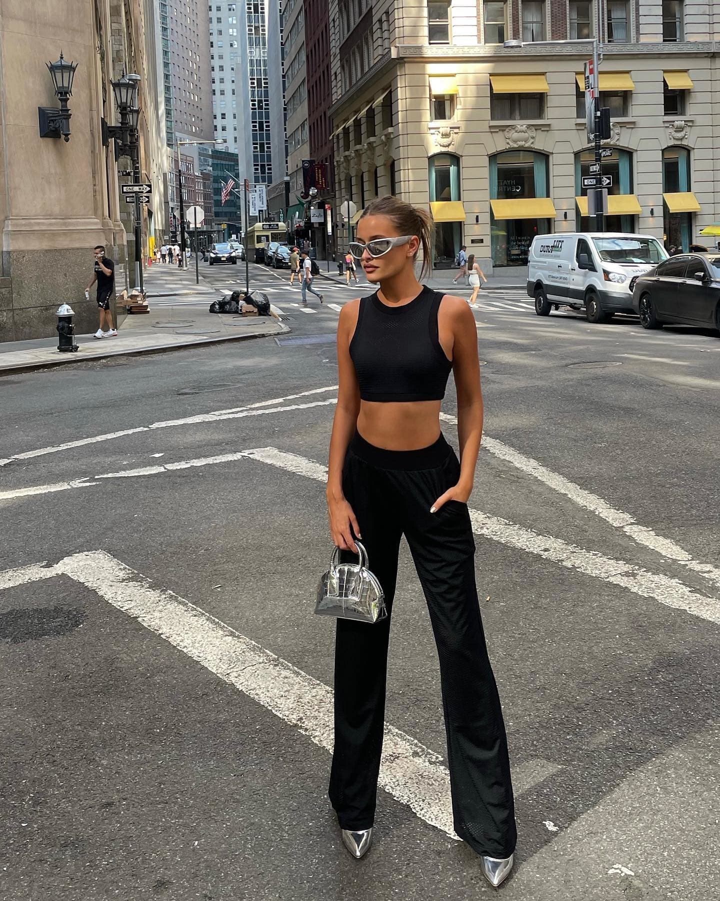 @lexiwood wearing an all-mesh matching set in black with a pair of chrome heels and matching small bag while standing in a crosswalk in a large city. 