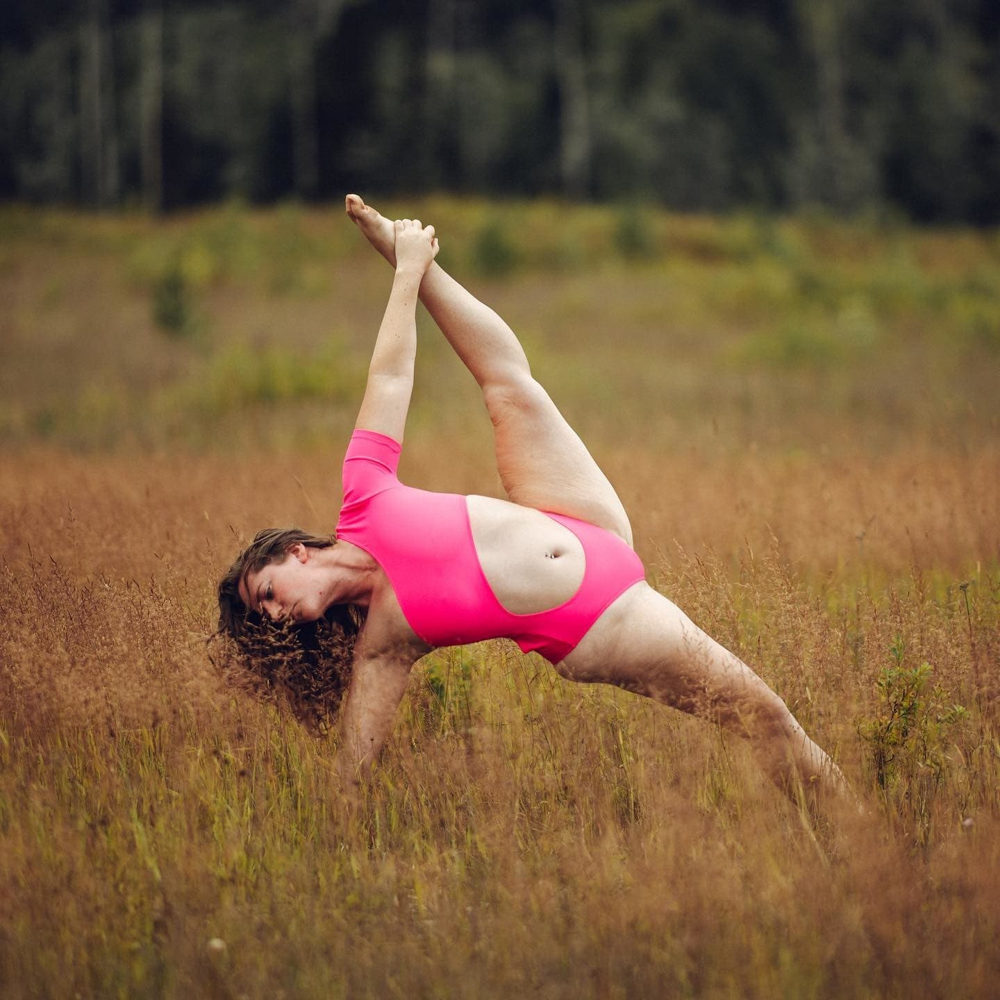 @vanessaeilene wearing a hot pink cut-out, one-sleeve bodysuit while stretching in an open field. 