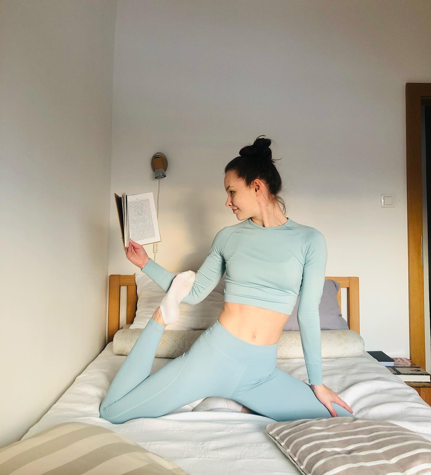 @wikybalance in a light blue set stretches on a bed while reading a book. 