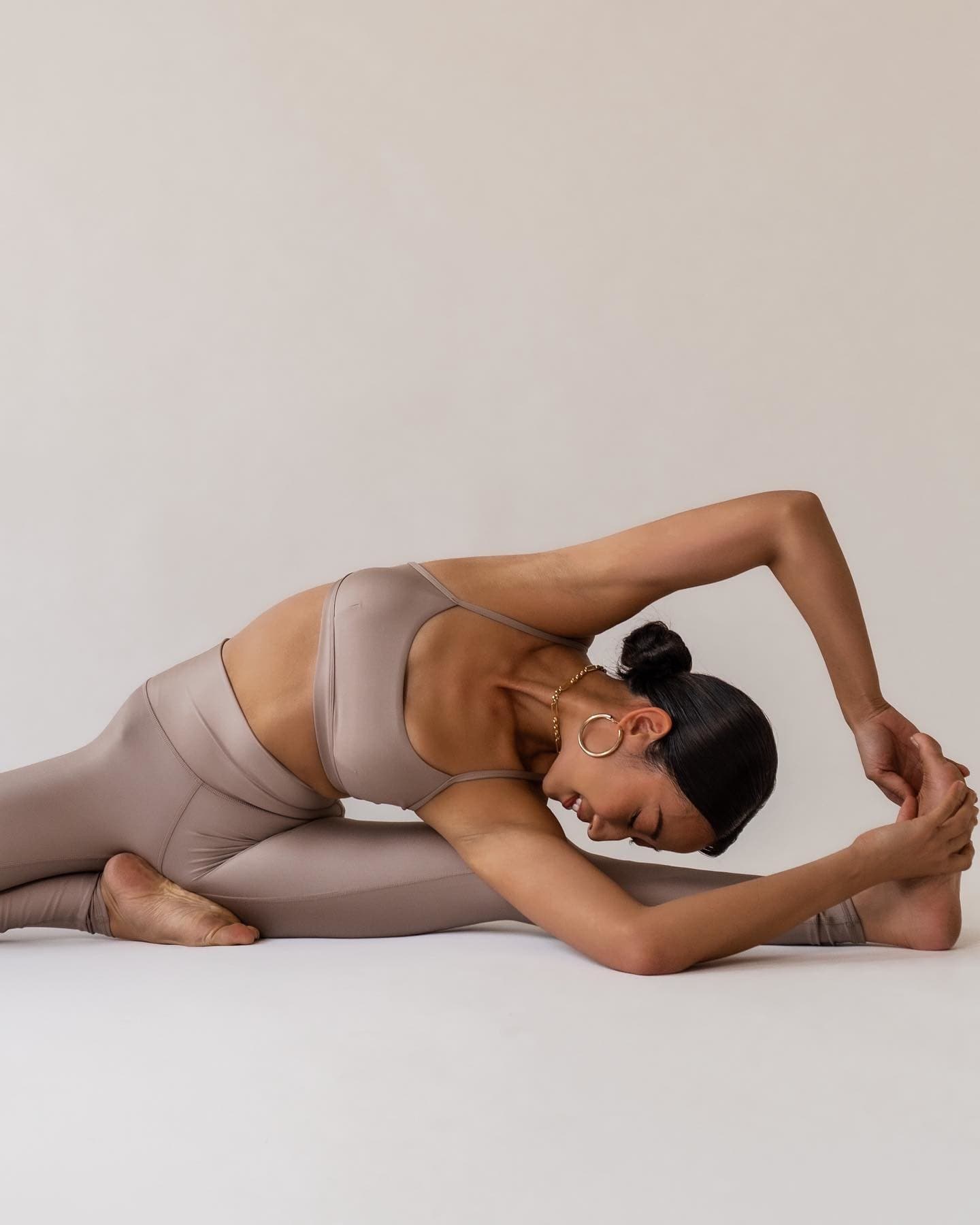 @yogibeachhouse wearing a matching workout set while stretching in front of a light taupe-colored background.  