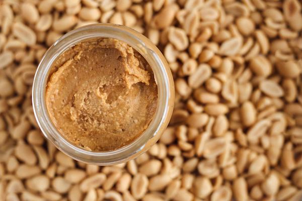 Jar of peanut butter with peanuts in the background