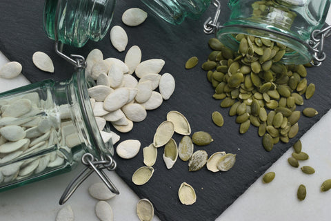 Two jars of pumpkin seeds spilled out onto a table.