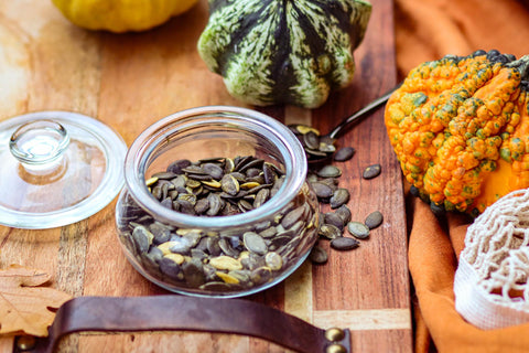 Pumpkin seeds in a jar surrounded by pumkins.