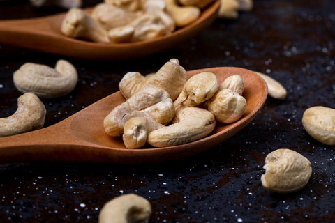 side view of wooden spoons with salted roasted pistachios on black background