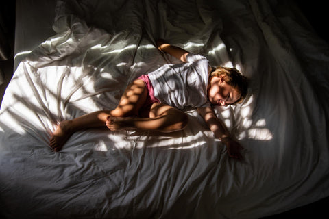 A child asleep on top of a bed covered by shadows.
