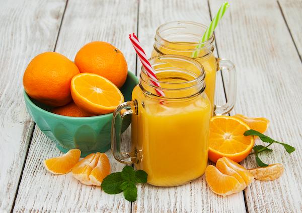 Orange juice in a jar next to a bowl of oranges cut in half