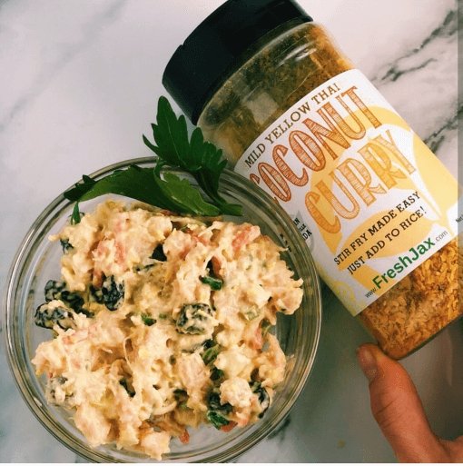 A bowl of coconut curry chicken salad next to a large bottle of FreshJax Organic Mild Yellow Thai Coconut Curry Spice.