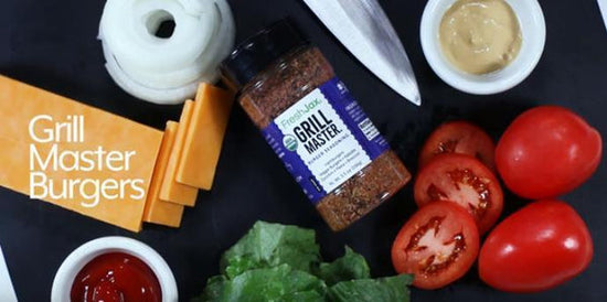 A large bottle of FreshJax organic grill master seasoning blend surrounded by burger ingredients including tomatoes, cheese, ketchup, onions, and lettuce. 