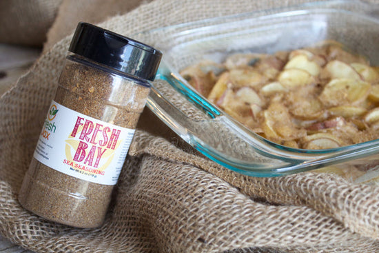 A bottle of FreshJax Fresh Bay Sea Seasoning next to a glass dish full of cooked scalloped potatoes.