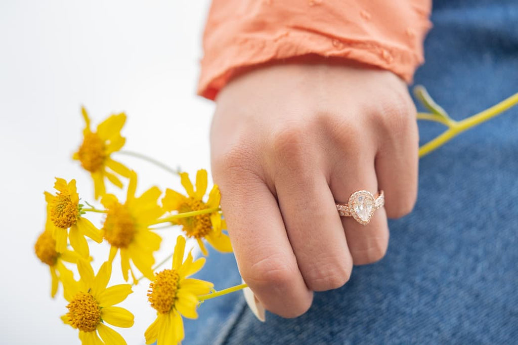 Woman's left hand holding yellow flowers wearing The Bliss set in rose gold on ring finger