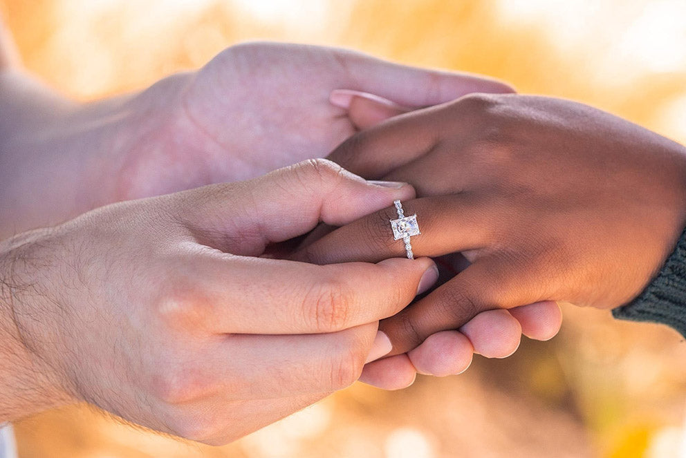 a man placing a thin band engagement ring on a womans finger
