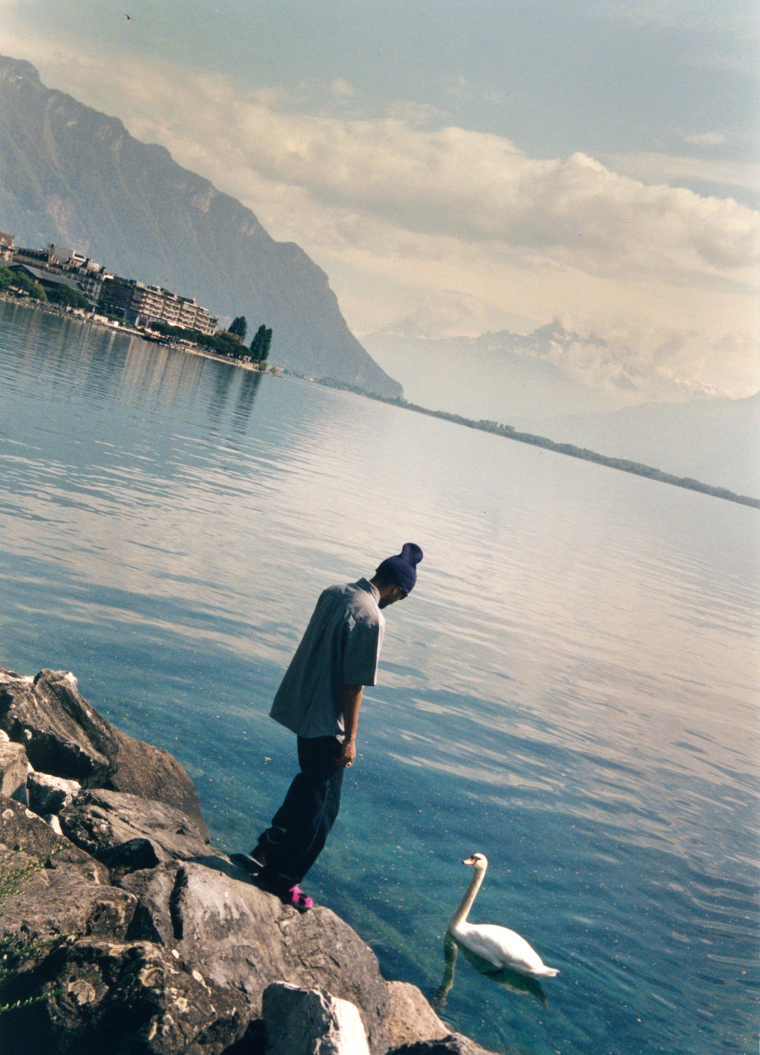 Wesley Joseph wearing Clink Heart Shirt in Wax, next to a duck in a lake valley of mountains.