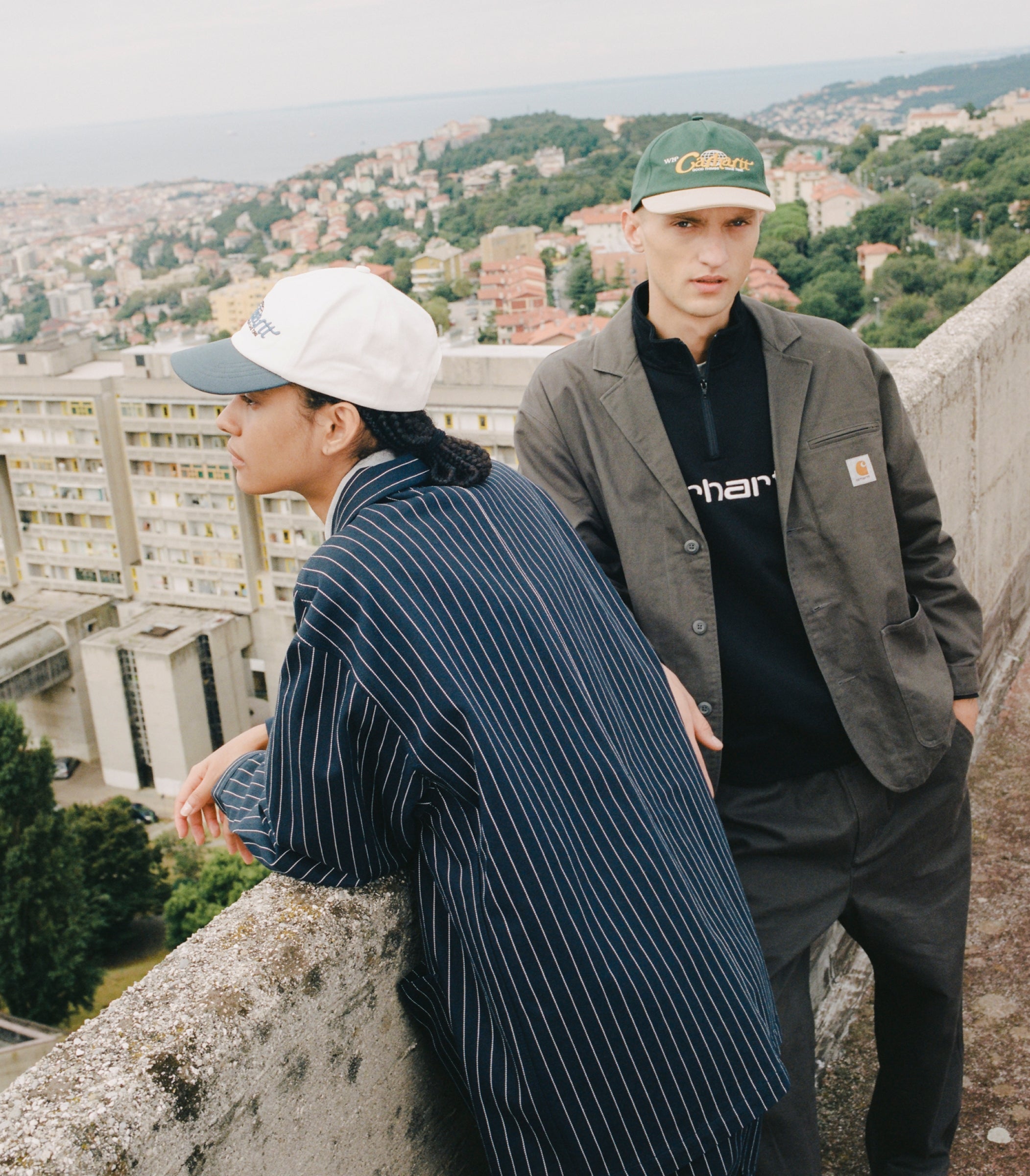 Models leaning over ledge wearing Carhartt WIP Hybrid Blazers in Dark Navy and Smoked Pearl