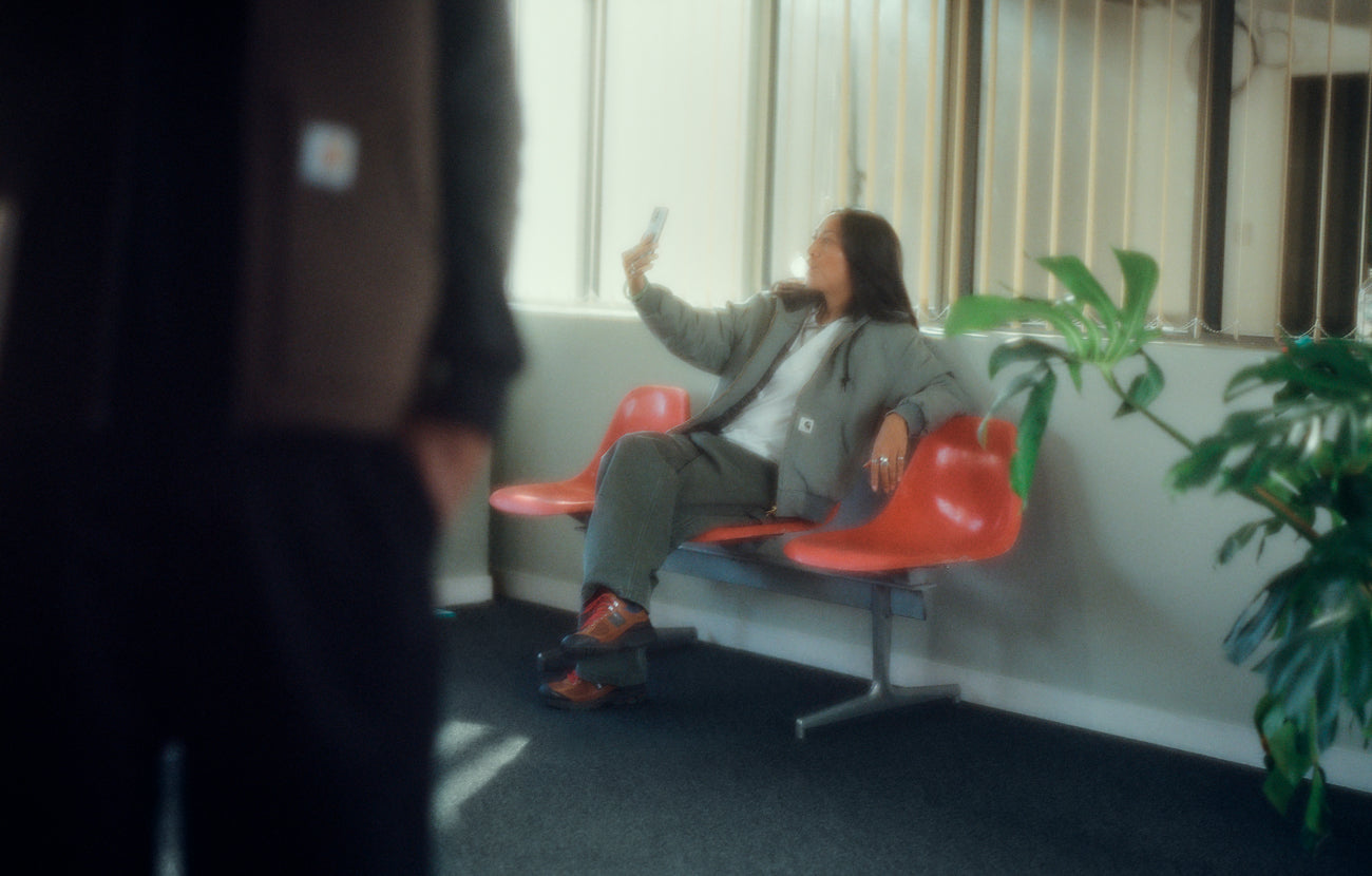 Model in waiting room holding phone wearing a Carhartt WIP Women's OG Active Jacket in Smoke Green