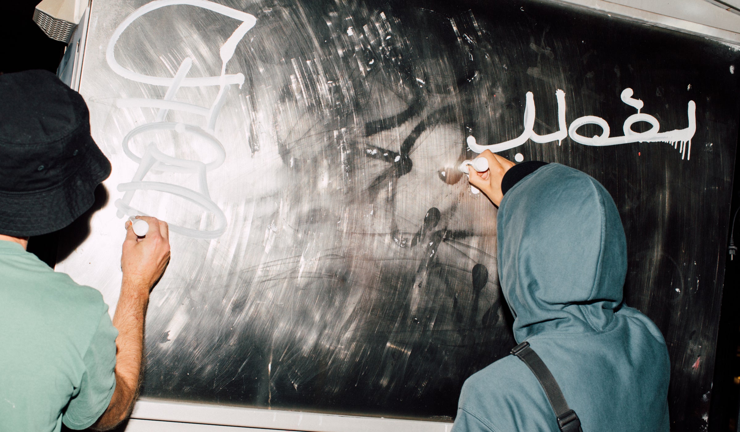 Two artist drawing on a black surface with Grog for Carhartt WIP Gel Markers in White