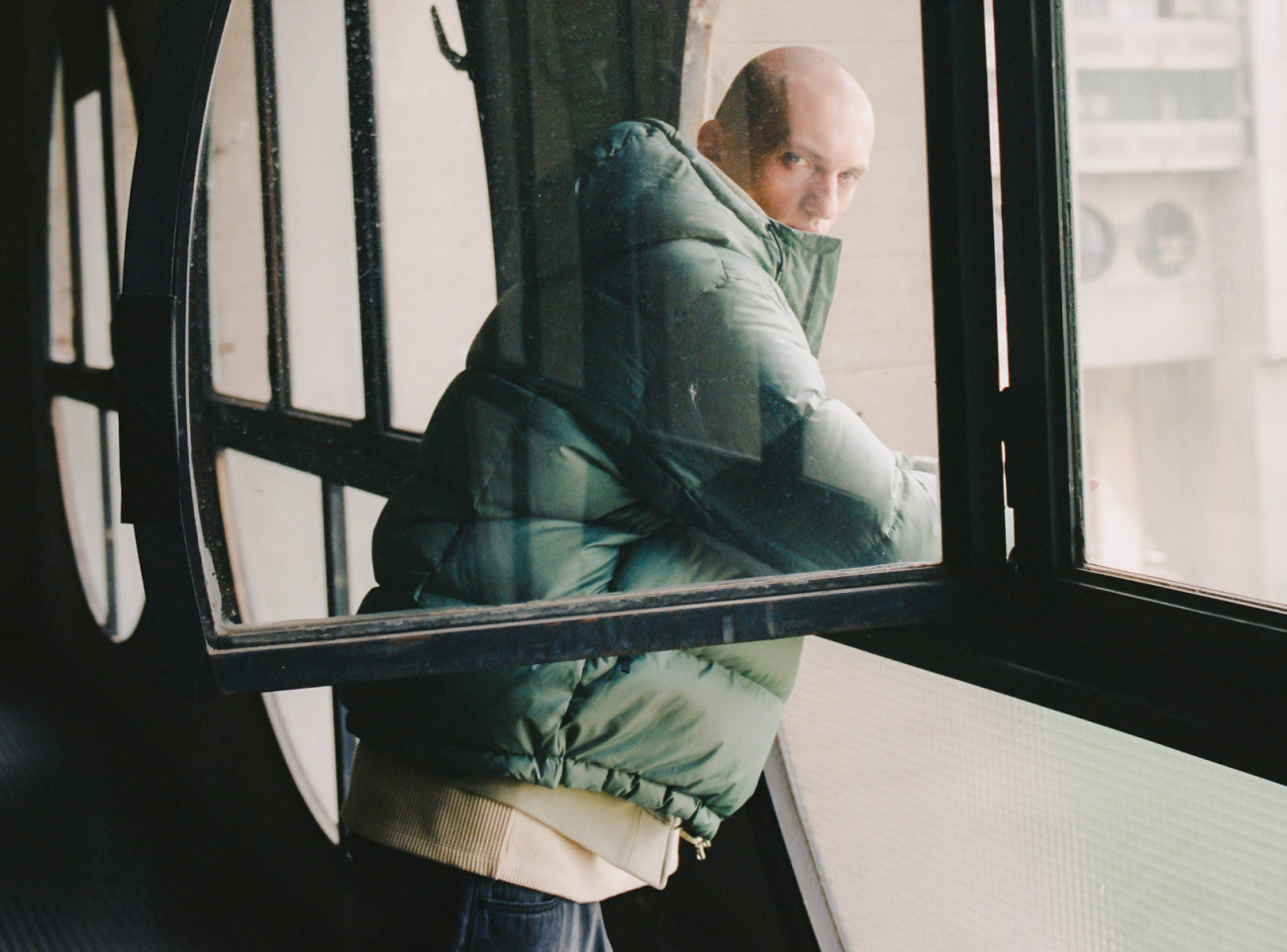 Model looking out of window wearing a Carhartt WIP Aspen Jacket in Alpha Green