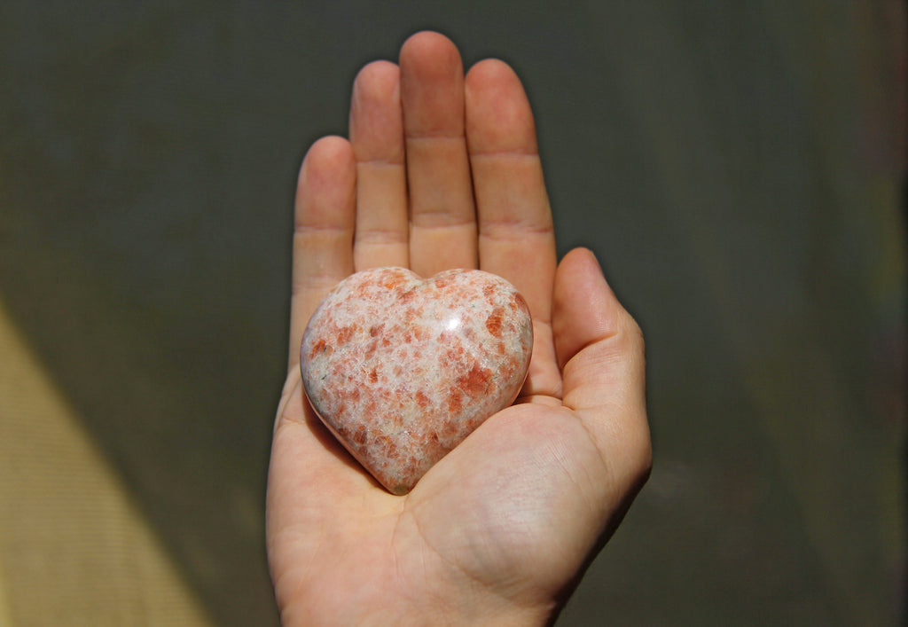 A hand holds a heart-shaped rhodochrosite stone