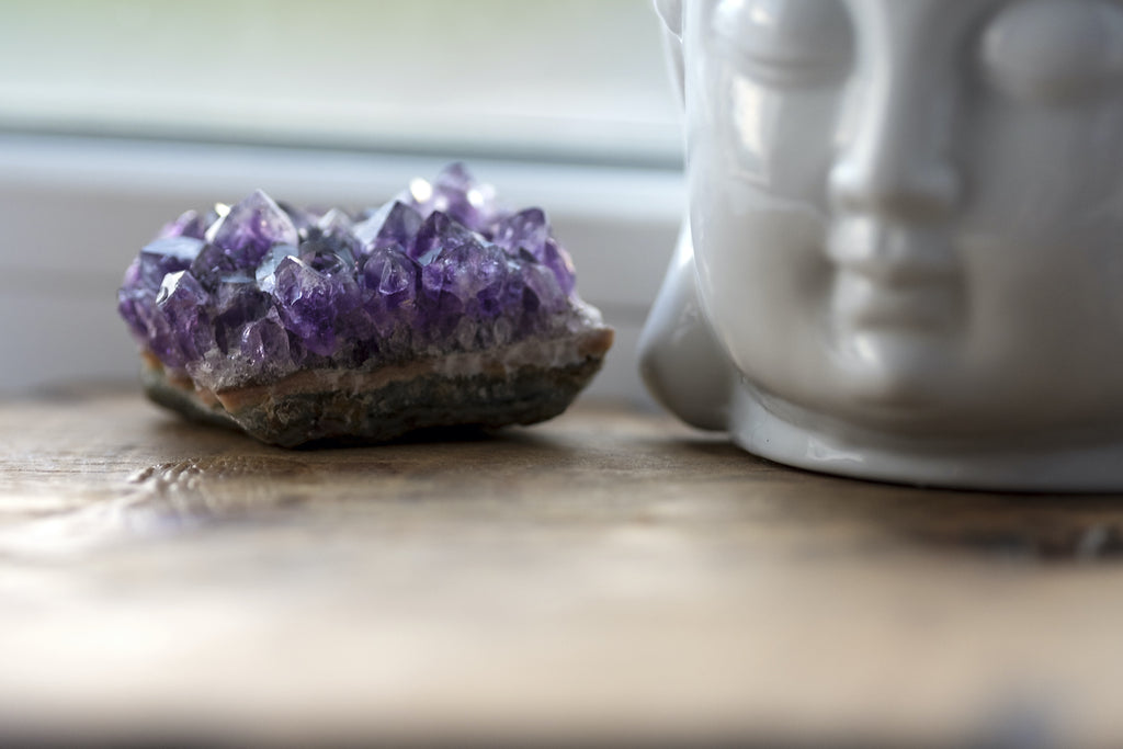 An amethyst crystal next to a sculpture of a buddha head