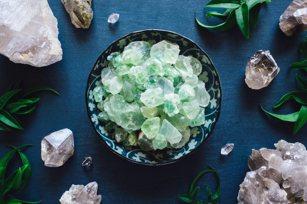 Zbiór kamieni zielonego fluorytu w misce, otoczony kwarcem i liśćmi paproci