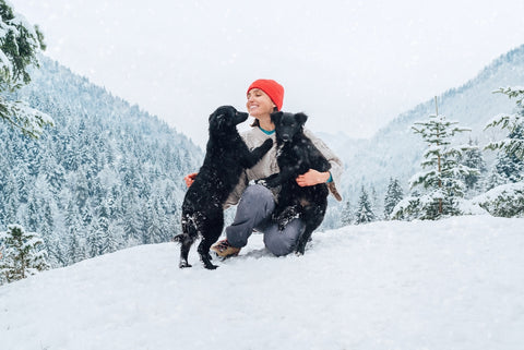 Smiling female human embracing black puppies playing in the snow