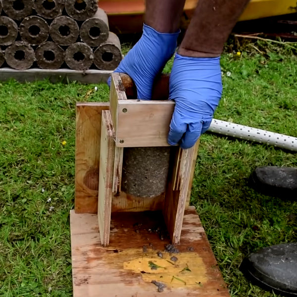 A man attempting to make his own biomass briquettes using a homemade manual pressing rod.