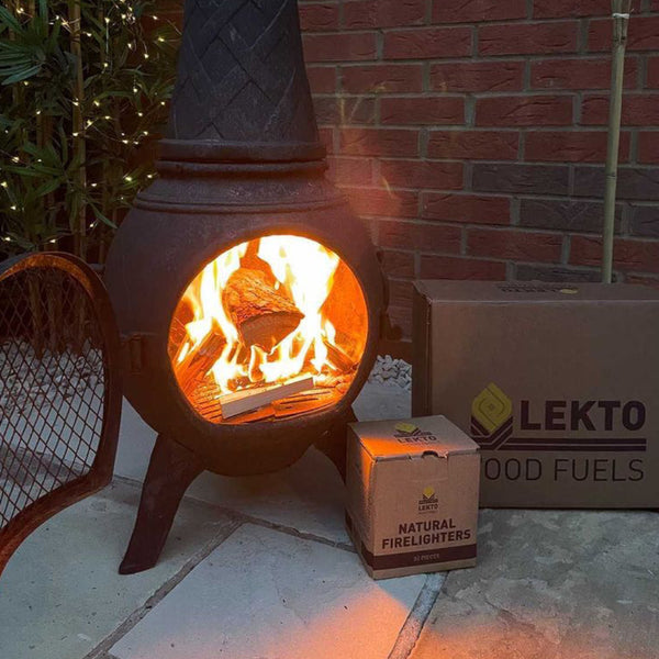 A cast Iron Chiminea with a lit fire next to a box of Natural Firelighters and a box of Wood Fuels 