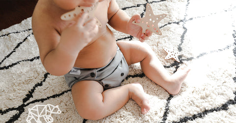 baby in grey cloth nappy, biting on a wooden star