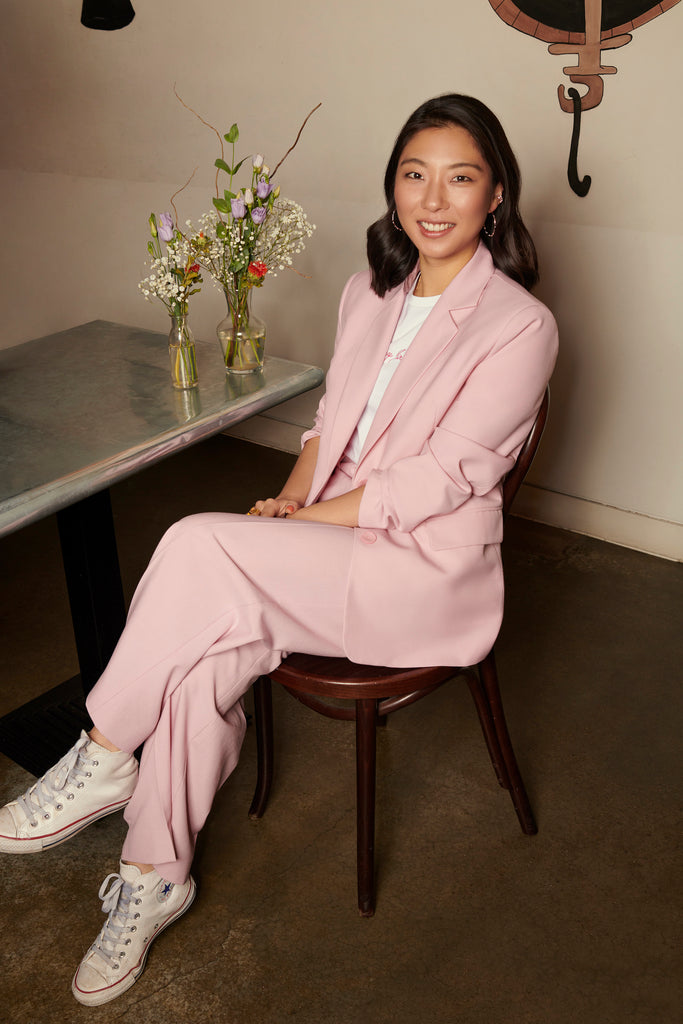 Photo of Haeni Kim sitting, wearing a pink suit with a white t-shirt, and white Converses