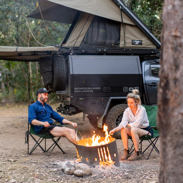 Borderland Explorers Matty and Em sitting at a campfire in front of their Isuzu Dmax, fitted with a Redback Exhaust