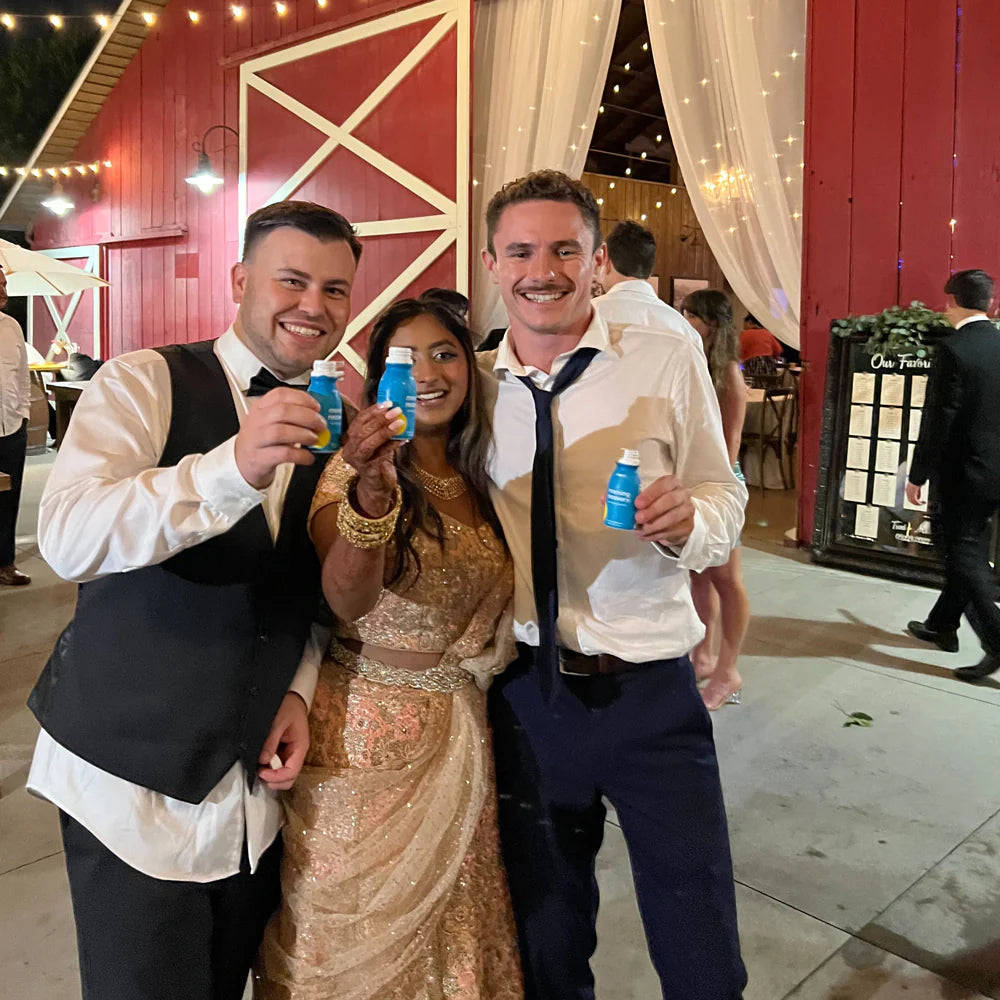 Guests celebrating at a wedding holding bottles of More Labs Morning Recovery dietary supplements.