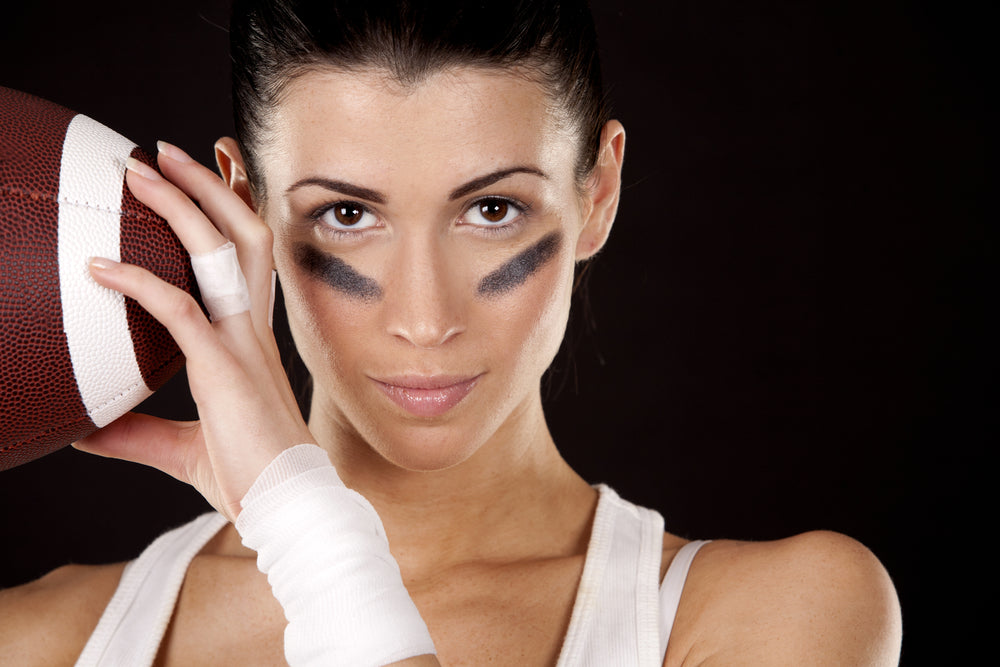 Woman holding a football with a bandaid on her ring finger and black stripes under her eyes