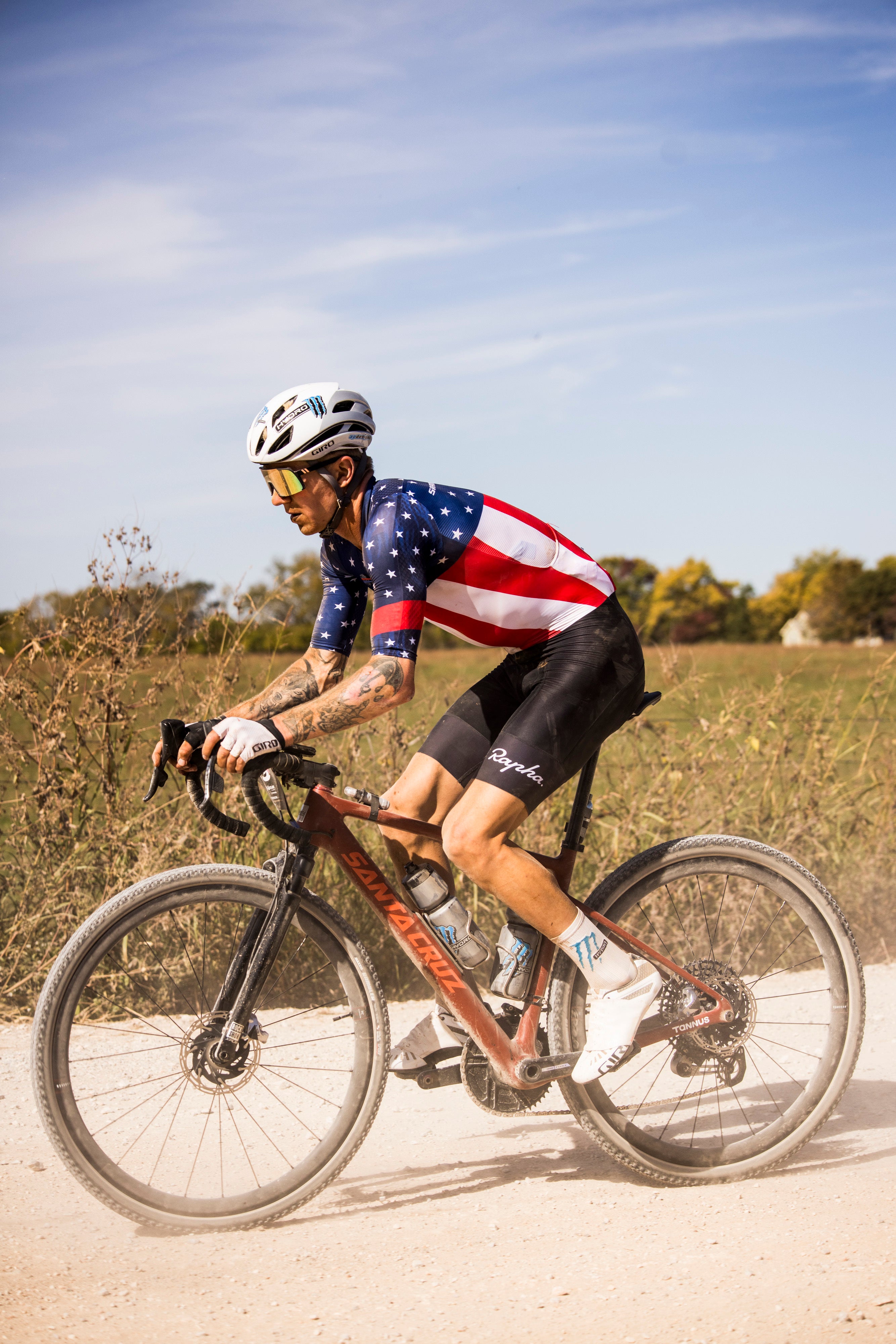 Keegan bikes a dusty road wearing an american flag biker suit. He looks focused.