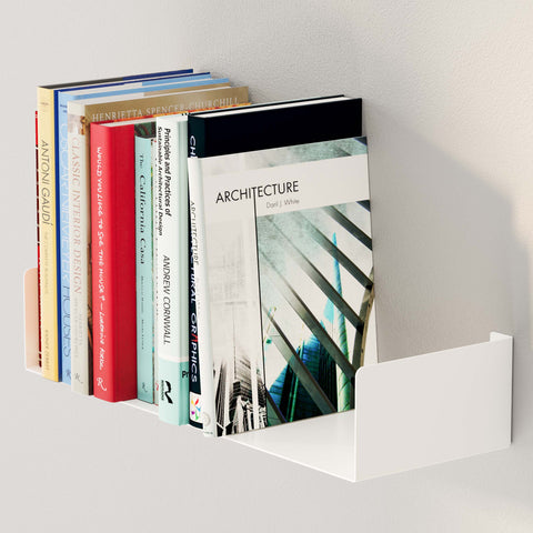 The image features a white metal U-shaped shelf mounted on a wall, holding a selection of books. The shelf has a clean, minimalist design, providing a modern and stylish storage solution. The books, including titles on architecture and design, are neatly arranged and supported by the U-shape's side panels, ensuring they stay upright. The shelf's sleek appearance and practical design make it an elegant addition to the space, perfect for organizing and displaying books or other items.