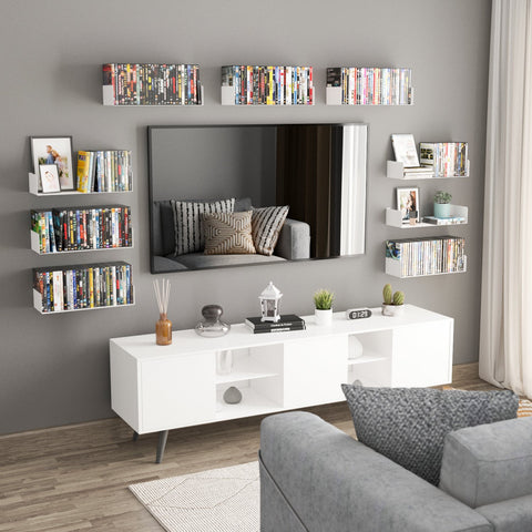 The image showcases a stylish living room with multiple white metal U-shaped shelves mounted on a gray wall. These shelves are filled with DVDs, books, and decor items. The shelves are arranged symmetrically around a large mirror, enhancing the room's modern aesthetic. Below the mirror, a sleek white console table holds additional decor, such as a clock, a lantern, and small plants. The arrangement is neat and visually appealing, making efficient use of wall space while adding a contemporary touch to the room's decor.