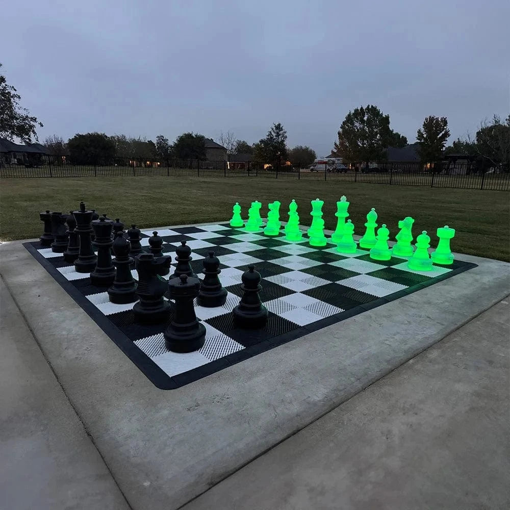 Chess set buying guide giant black and glowing green LED chess set on outdoor black and white checkered board at dusk with grassy field and trees in background.