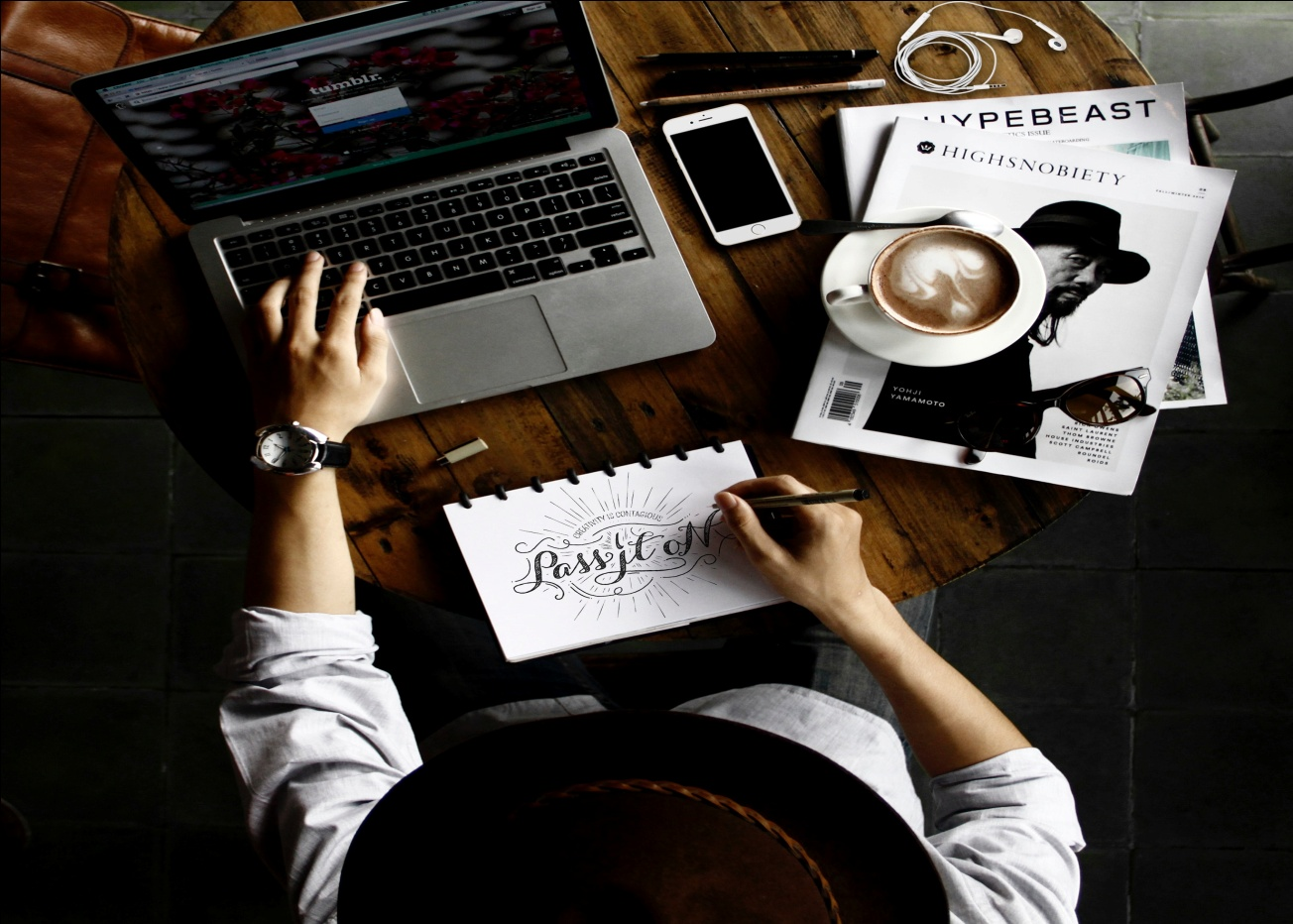 Person sitting facing a laptop with a sketch pad Person sitting with a sketch in front of an open laptop