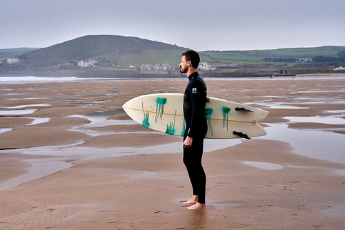man in a wetsuit holding a surf board on the beach