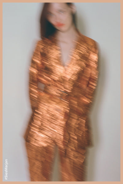 Blurry image of model wearing Sies Marjan Terry Metallic Belted Blazer in Pumpkin color. Shot by Theo Wenner.