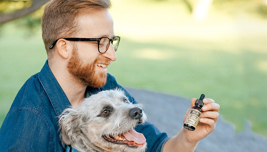  Man  smiling and holding his dog and CBD Oil