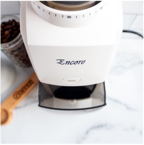 White Encore burr grinder with a mason jar of beans and a measuring spoon on a white marble counter
