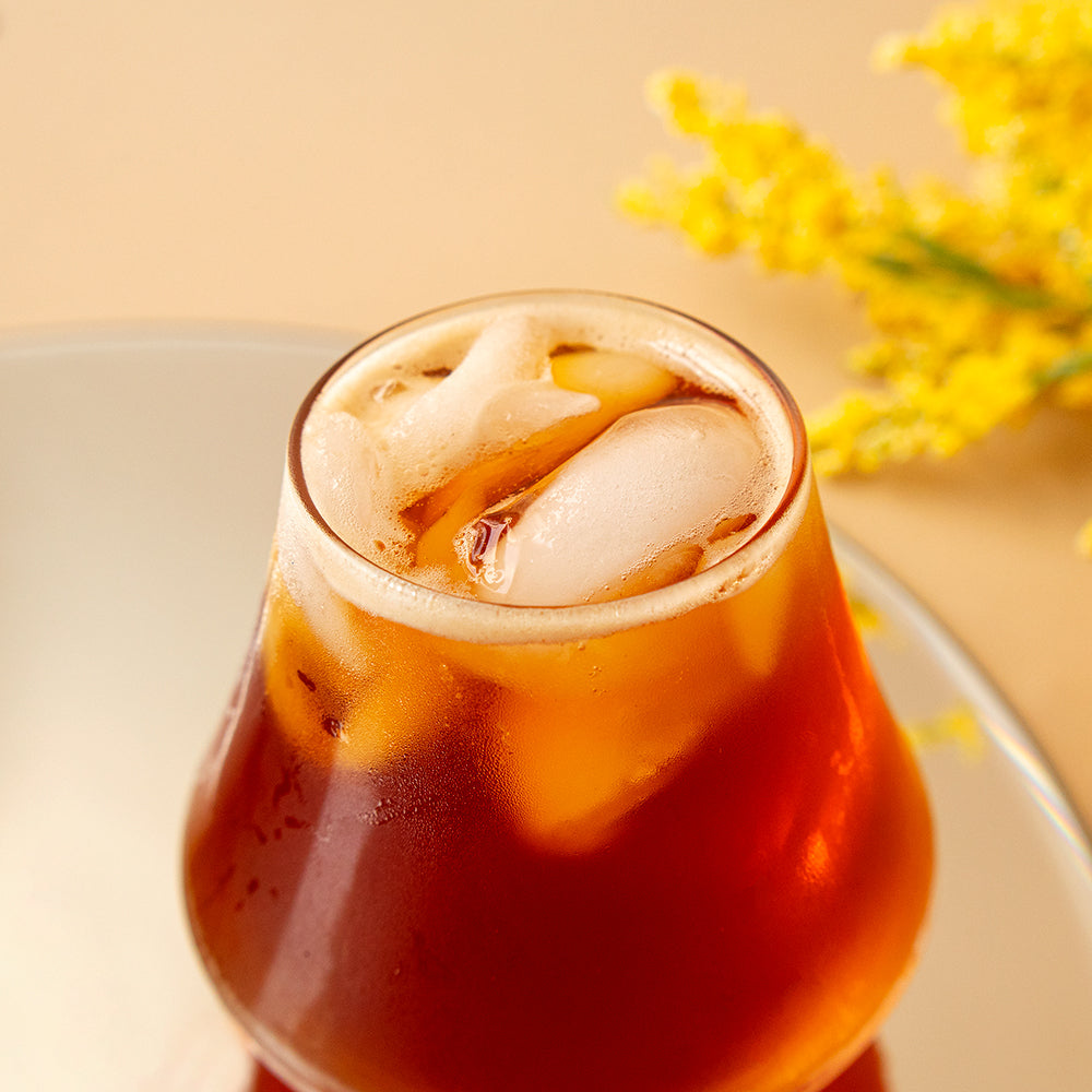 A glass of black tea on a mirror in front yellow foliage.